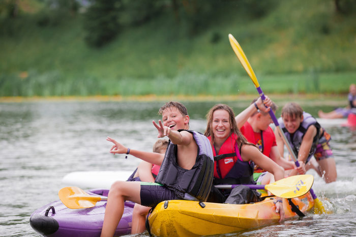 Grupo de participantes de los campamentos de verano en Austria sonrientes mientras practican kayak en un lago