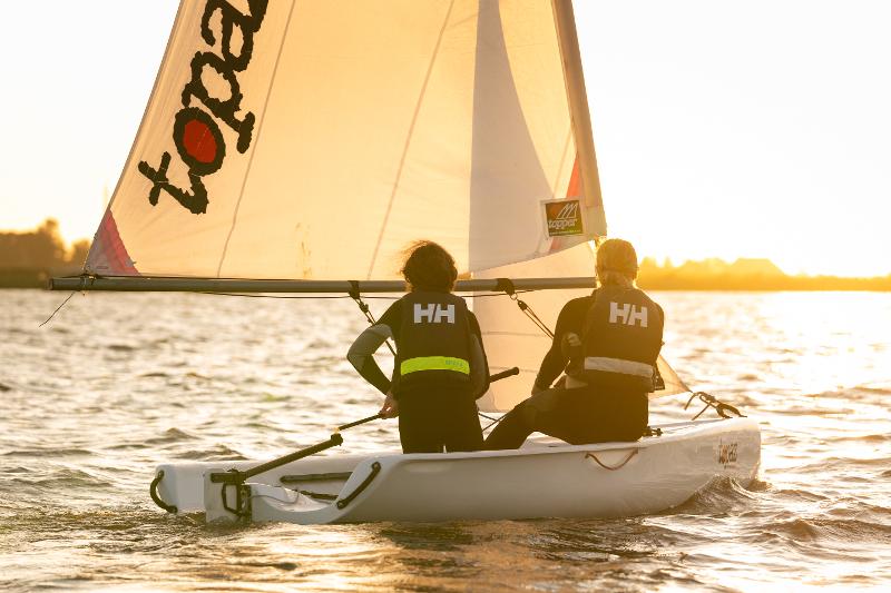 Jóvenes navegando con el atardecer de fondo durante el camapmento de verano en holanda