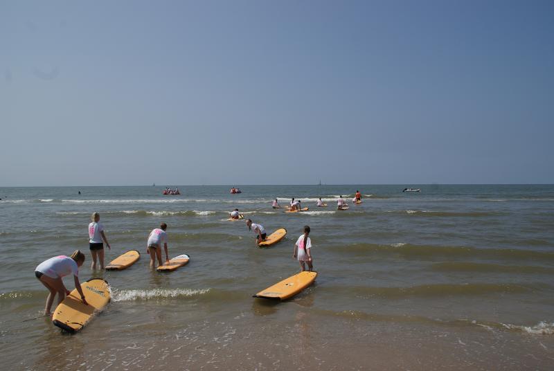 Jóvenes entrando al mar con sus tablas de surf en el campamento de verano en Holanda