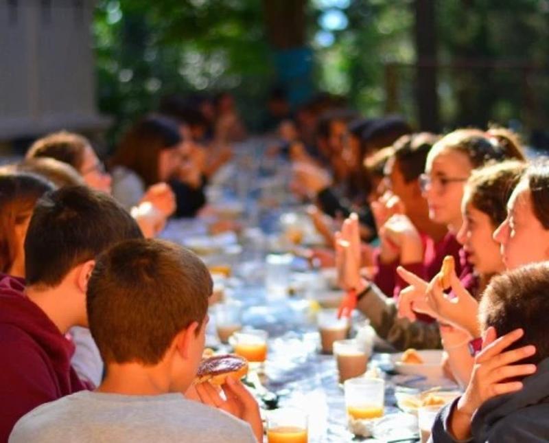 Chicos y chicas desayunando en el campamento
