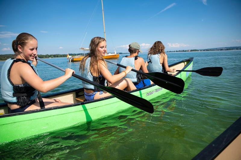 Grupo de cuatro chicas jóvenes disfrutando de un paseo en piragua en el lago del campamento de verano en Países Bajos