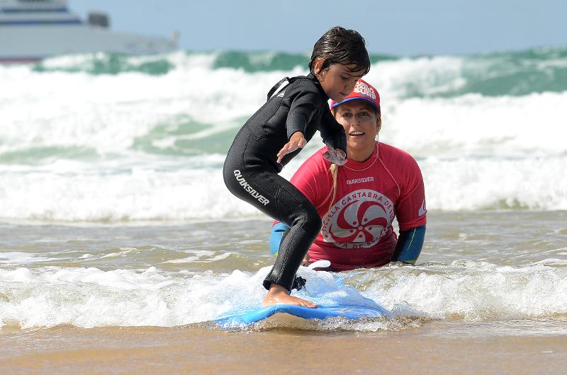Niño practicando surf en la playa del campamento de verano en Cantabria