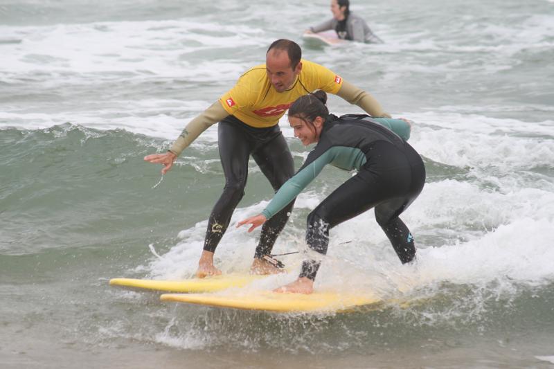 Niña practicando surf con el monitor en la playa en el campamento de verano en cantabria