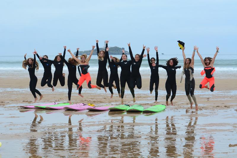Chicas saltando en la playa junto a sus tablas en surfcamp en cantabria