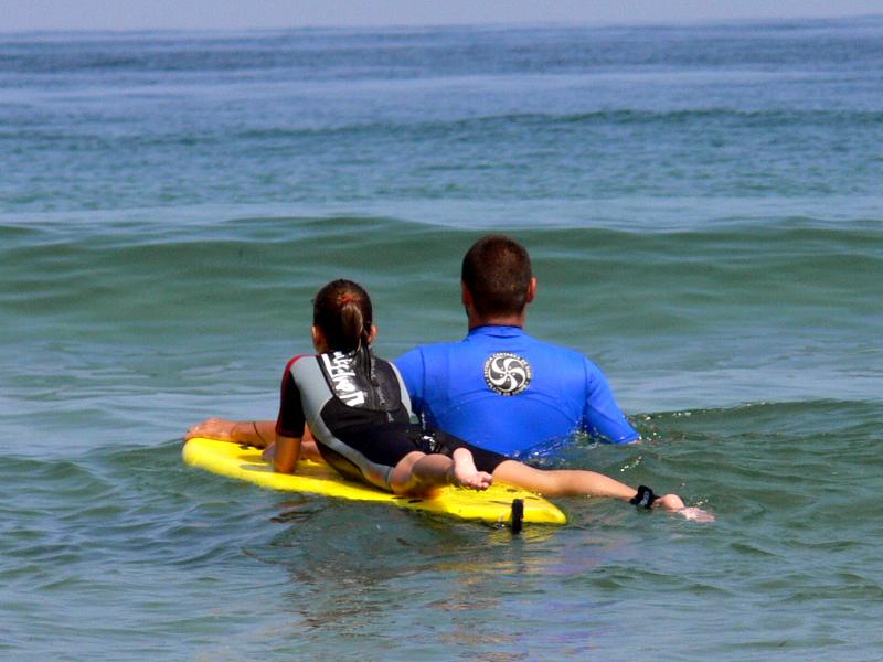 Monito y niña de espaldas en el agua aprendiendo a surfear en surfcamp en cantabria