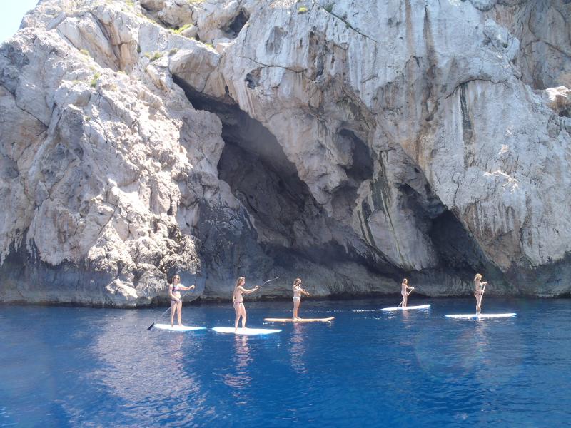 Chicas de pie en sus tablas en el mar azul junto a las cuevas rocosas en surfcamp en cantabria