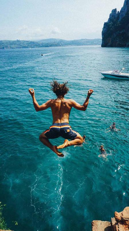 Adolescente saltando al mar durante un campamento ingles verano Cantabria