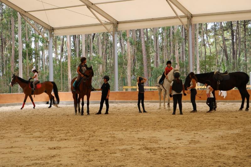 jovenes y niños montando a caballos y supervisando las clases de hipica en el campamento de verano en portugal