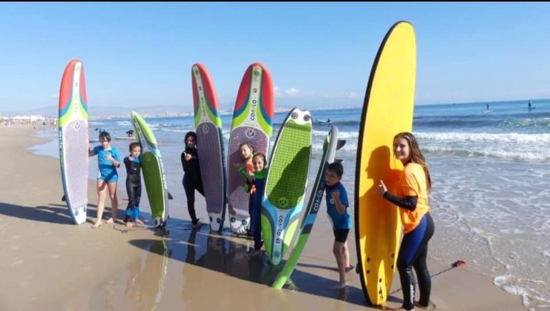 Niños en la playa sujetando sus tablas de surf en la orilla en el campamento verano alicante