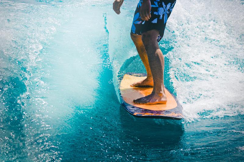 Las piernas de un campista sobre la tabla de surf en el mar en el campamento verano alicante