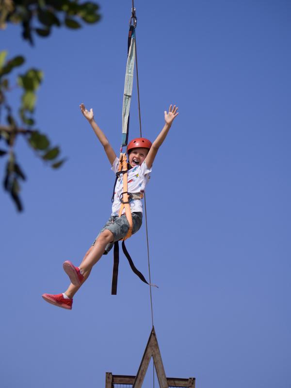 Niña con arnés levantando los brazos mientras está en la tirolina en el campamento verano alicante