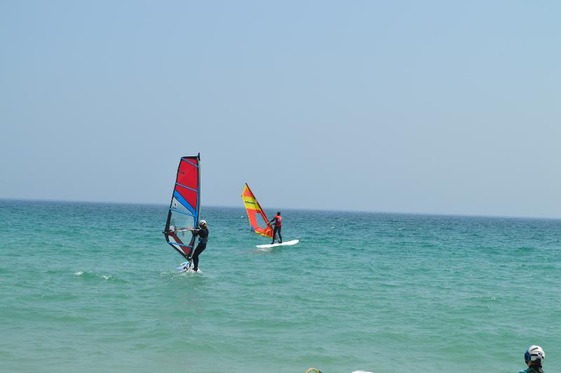 Jóvenes practicando Windsurf en la playa con la supervisión del monitor del campamento de verano en Cádiz