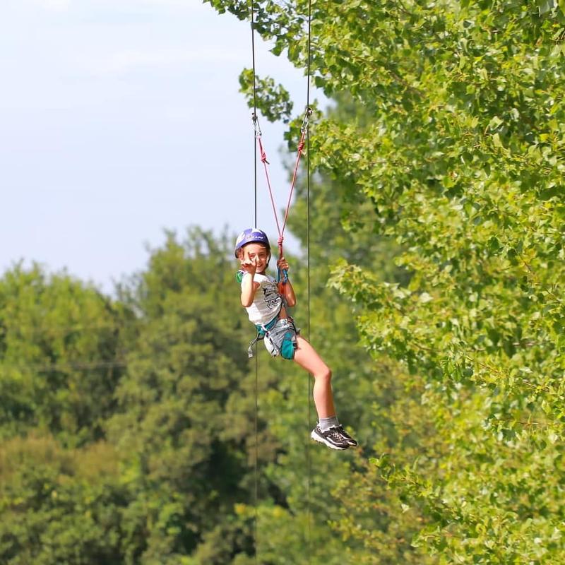 Jeune fille avec baudrier et casque fait de l'accrobranche en colonie sportive été