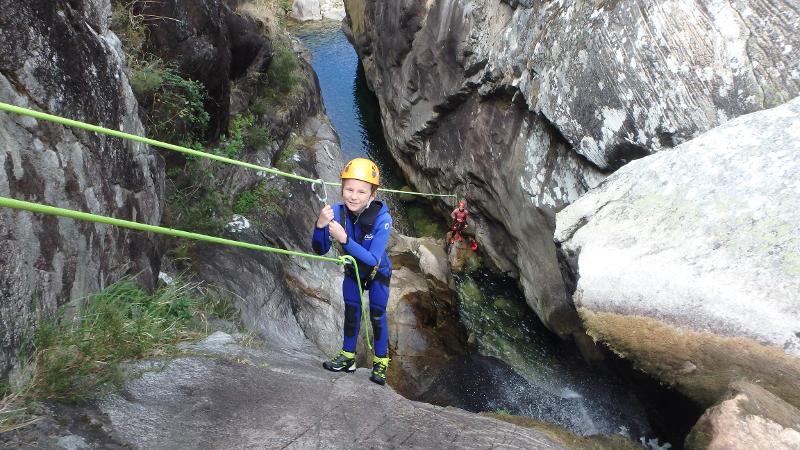 Participante infantil vestido con equipación deportiva agarrado aun mosquetón mientras precticas escalada en el campamento en Suiza