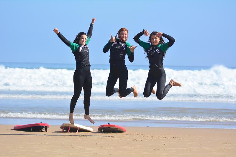 Jóvenes en la playa saltando y disfrutando del día de surf en el campamento de verano en Cantabria