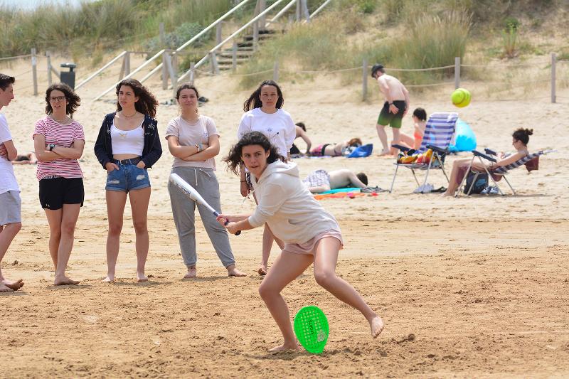 Chica preparada para chutar la pelota en un partido de béisbol en la playa bajo la atenta mirada de sus compañeros del campamento de verano en Cantabria
