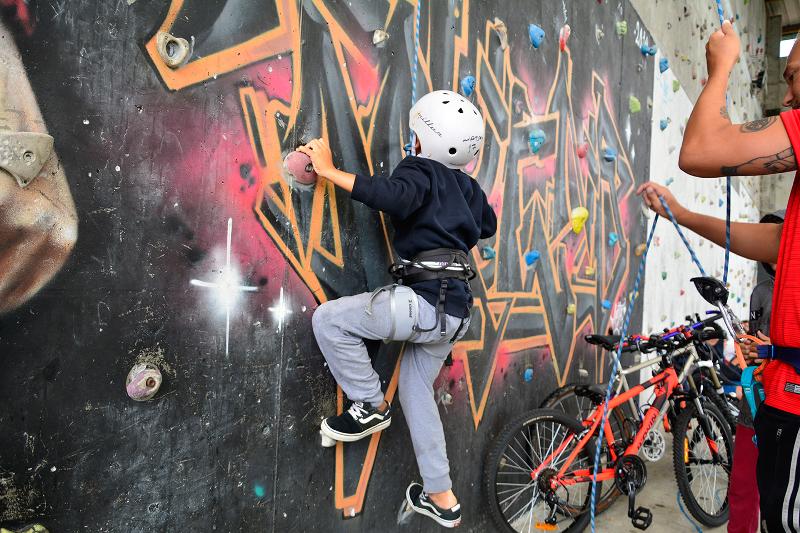 Niño haciendo escalada en el rocódromo con la ayuda del monitor del campamento en Cantabria