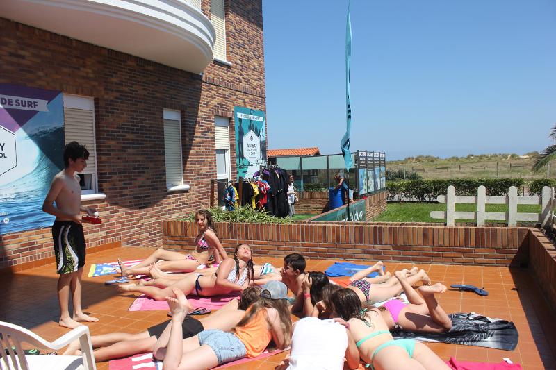 Grupo de jóvenes tomando el sol en la terraza del campamento de surf en Cantabria