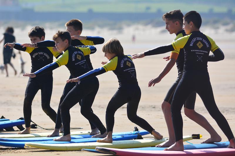 Grupo de niños practicando en la arena las técnicas de surf en el campamento de verano en Cantabria