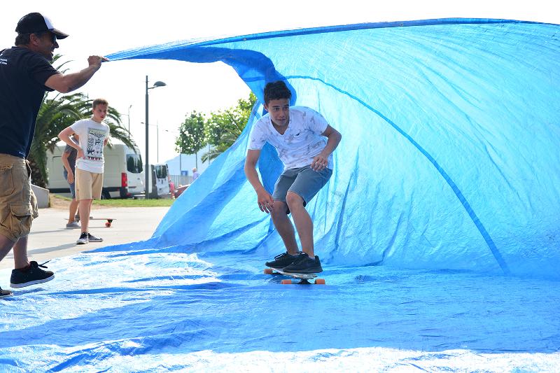 Joven realizando skate bajo una lona azul sujetada por uno de los monitores del campamento de verano en Cantabria