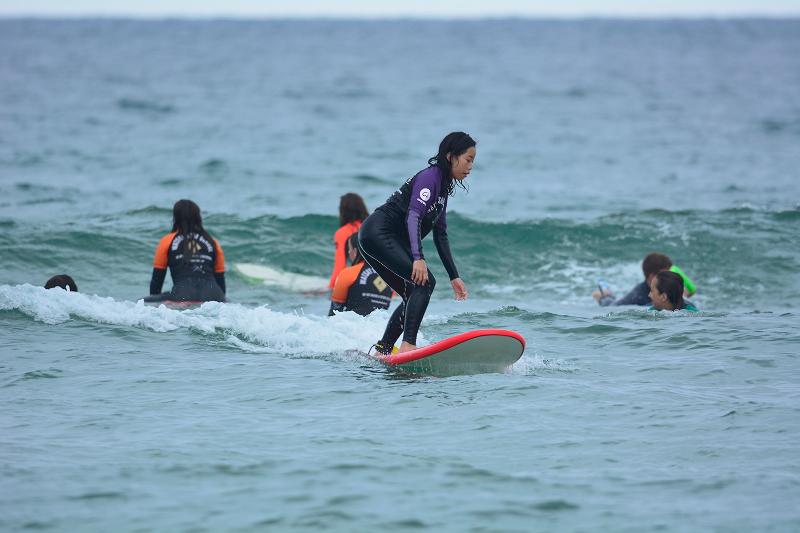 niña haciendo surf y otras niñas esperando las olas en el campamento verano Marbella