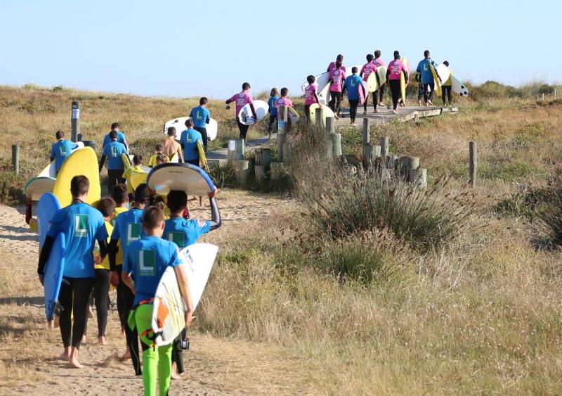 Grupo de jóvenes caminando en fila hacia la playa para las clases del campamento de surf en Cantabria
