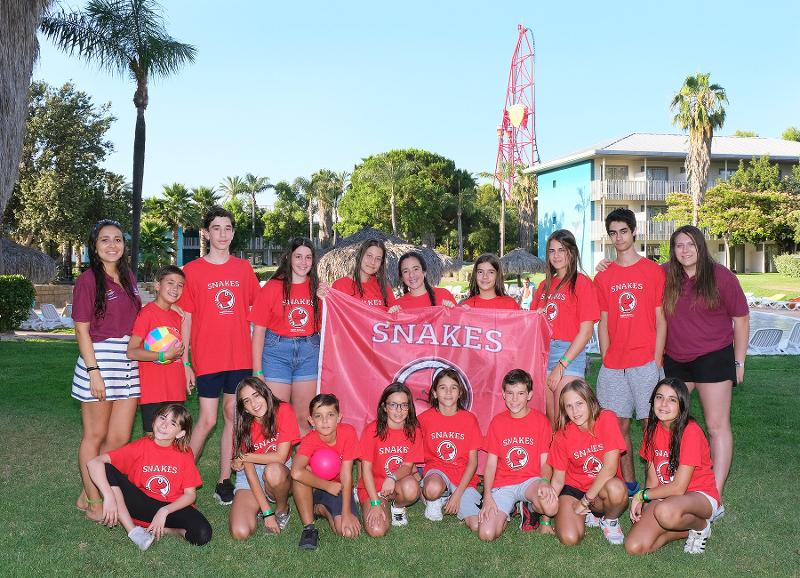 Grupo de jóvenes posando con una bandera en las instalaciones del parque de atracciones de port aventura durante el campamento de verano Navarra