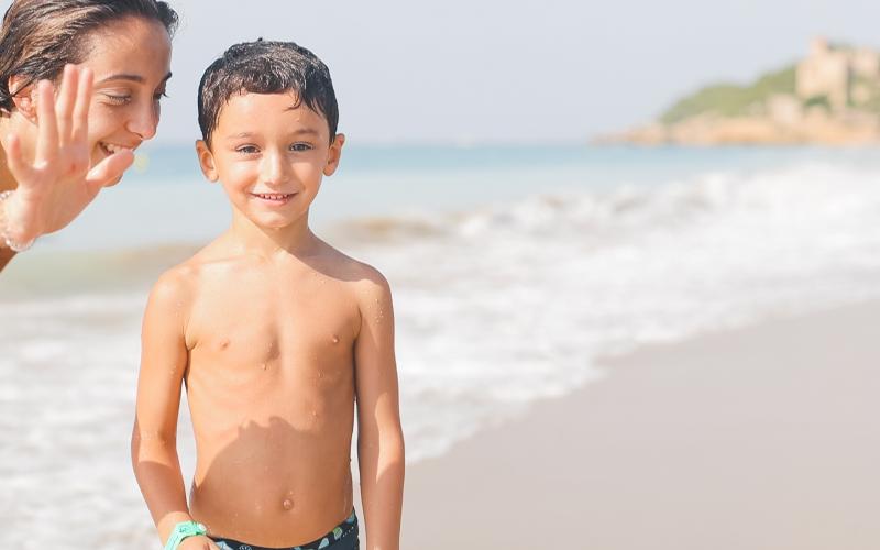 Niño feliz en la orilla de la playa en un dia de actividades acuaticas del campamento de verano en tarragona