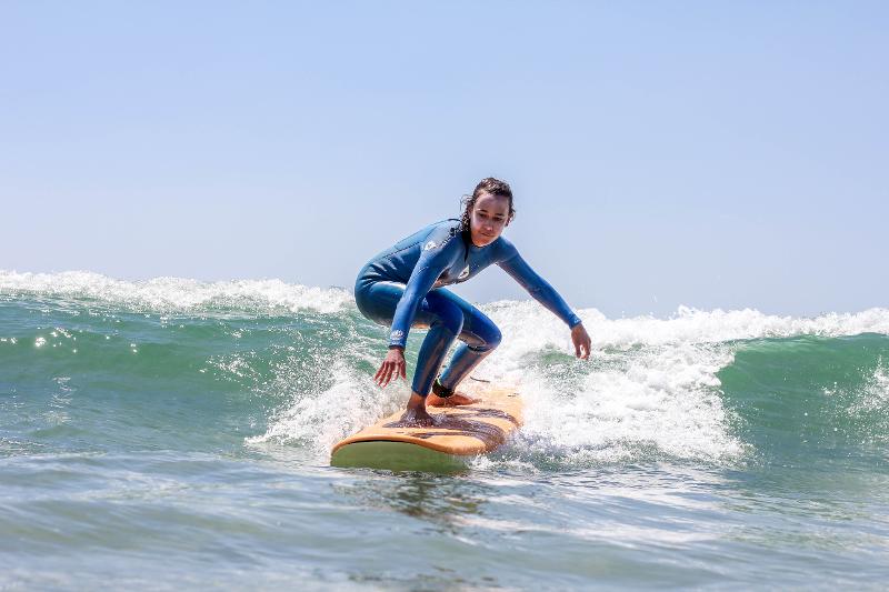 Chica joven con neopreno azul surfeando una ola sobre la tabla del campamento de surf Somo