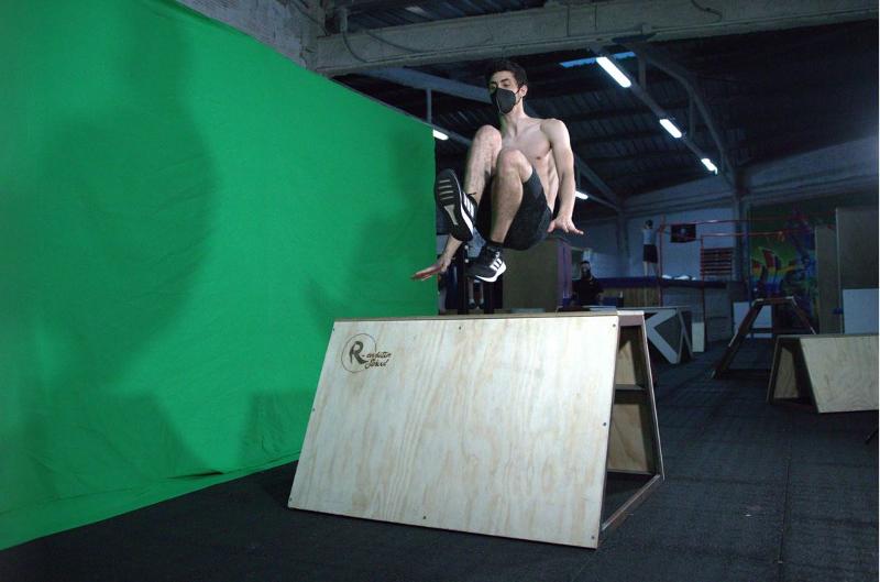 Chico joven adolescente saltando una rampa de madera en el campamento de parkour probando nuevos trucos