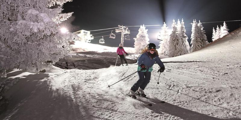 Participantes de las vacaciones de ski bajando una pista de noche