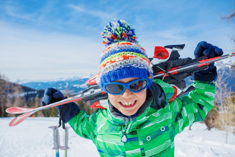 Niño sonriente con el atuendo de esquí sosteniendo unos bastones en las vacaciones ski