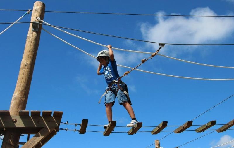 Niño en el campamento de verano montaña disfrutando de las actividades de tirolinas y circuitos de cuerdas