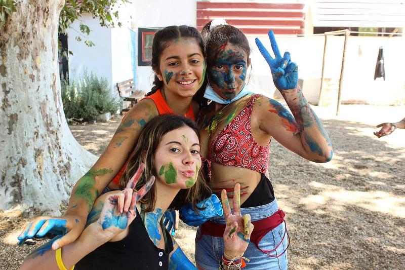 Tres niñas sonrientes con la cara pintada disfrutando de una actividad artística en el campamento Suiza