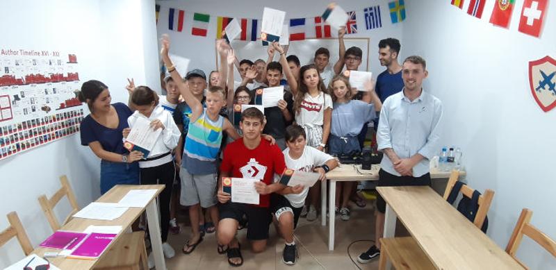 Grupo de niños y niñas en un aula enseñando sus diplomas tras haber completado el campamento de verano Alicante