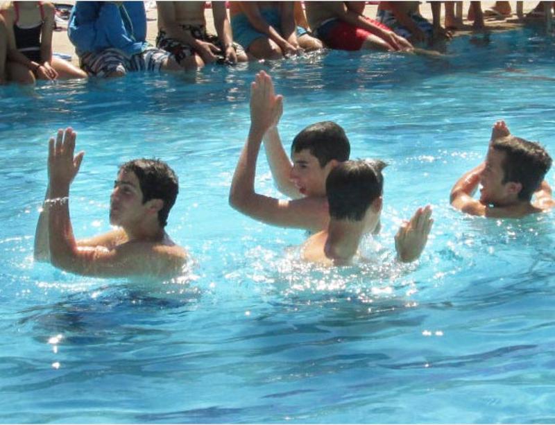 Grupo de cuatro jóvenes aplaudiendo dentro de la piscina del campamento de verano en Madrid
