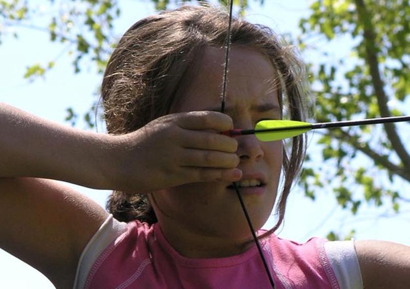 Niña practicando tiro con arco en el campamento de aventuras en Madrid