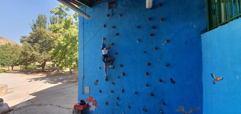 Joven escalando en el rocódromo preparado por el campamento de verano en Madrid