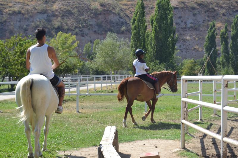Joven montando a caballo en la clase de hípica con el instructor del campamento con animales en Madrid