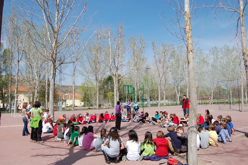 Grupo de jóvenes sentados en circulo escuchando a uno de los monitores explicando el juego a realizar en el campamento de verano en Madrid