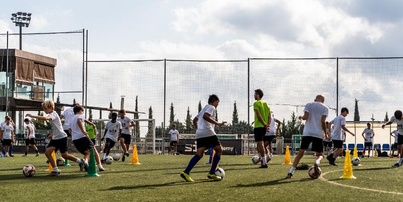 Adolescentes realizando un ejercicio con conos en un campamento de futbol