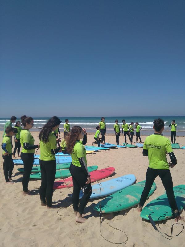 Grupo de participantes del campamento de surf en ingles realizando una clase de surf en la playa