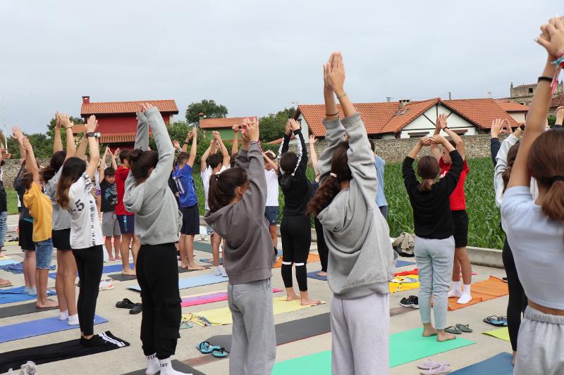Participantes realizando una clase de yoga al aire libre en el campamento de surf en ingles