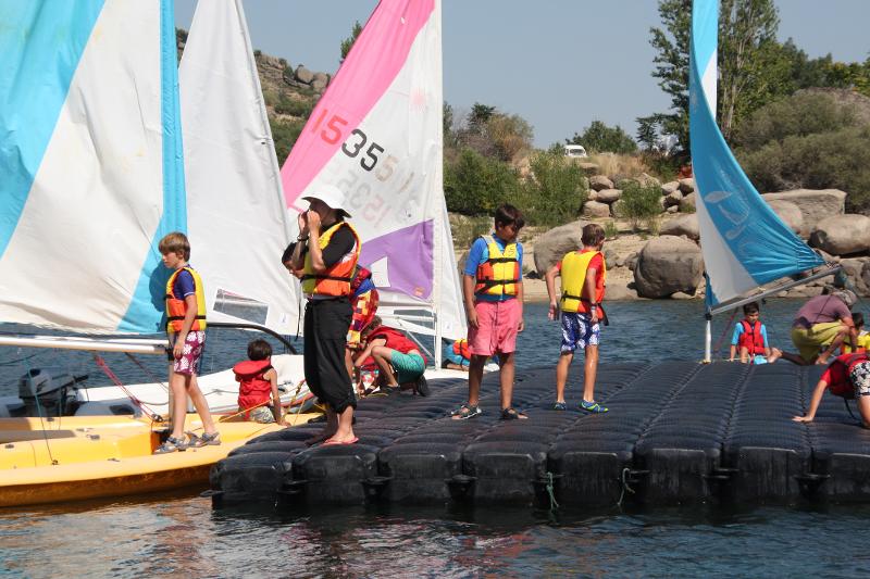 Niños encima del muelle preparándose para montarse en los barcos en el campamento vela