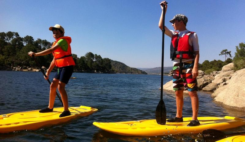 Dos niños haciendo paddle surf en el embalse en las actividades acuáticas del campamento madrid