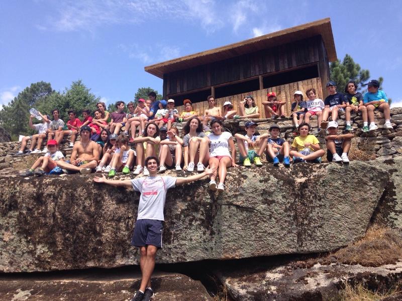 Grupo de niños sentados encima de una roca posando junto con su monitor en una excursión del campamento vela