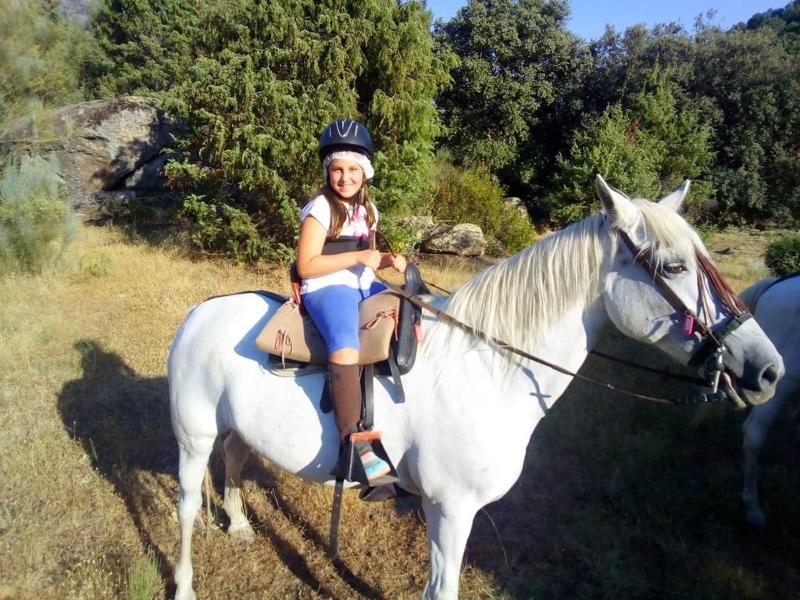 Niña montando a caballo en una excursión por la naturaleza que rodea el campamento de verano en Madrid