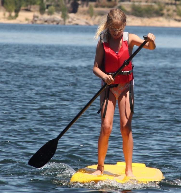 Niña remando su tabla de paddle surf en el embalse en las actividades deportivas del campamento madrid