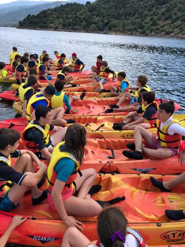 Grupo de niños sentados por parejas y tríos en los kayaks preparados para los deportes acuáticos del campamento nautico