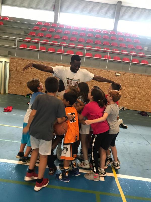 Niños abrazando a su entrenador durante un campamento de baloncesto